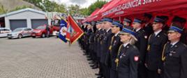 Zdjęcie przedstawia pododdziały strażaków oraz poczty sztandarowe PSP i OSP z powiatu Zgierskiego, w tle widać pojazdy pożarnicze