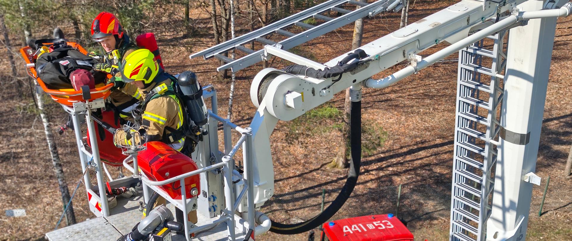 Zdjęcie przedstawia podjęcie poszkodowanego z wysokości za pomocą podnośnika strażackiego.