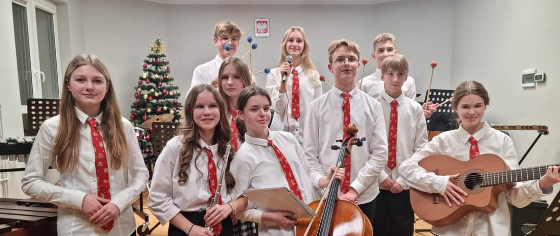na zdjęciu grupa młodzieży w białych koszulacj i czerwonych krwatach z instrumentami w rękach