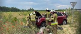 Czterech strażaków wokół rozbitego samochodu na poboczu
