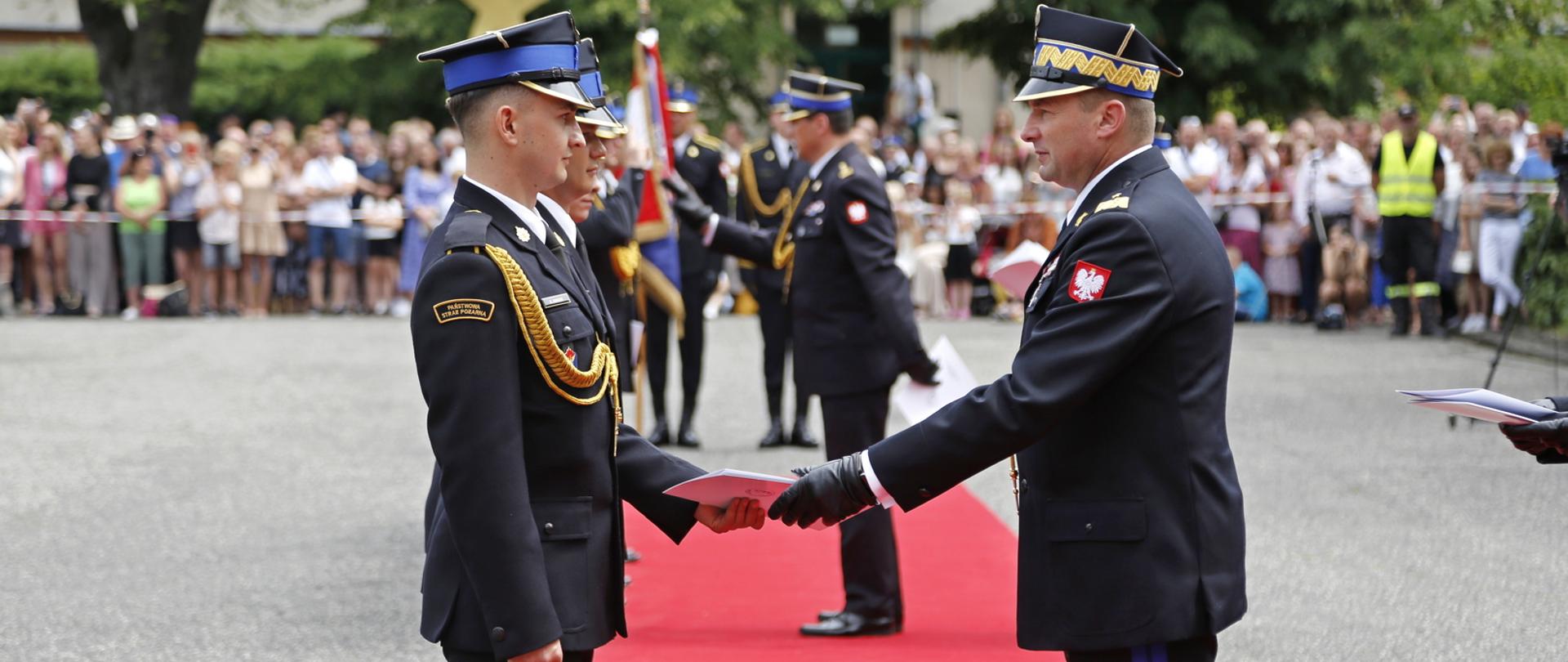 Zastępca komendanta głównego PSP wręcza teczkę z aktem promocji strażakowi