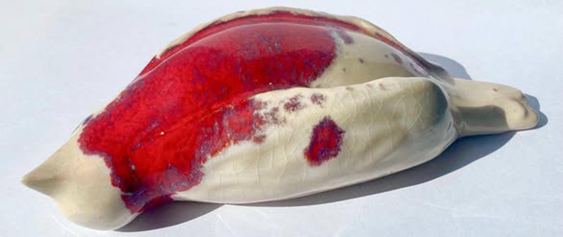 Rzeźba ceramiczna przedstawiająca leżącego białego gołębia z czerwoną plamą.