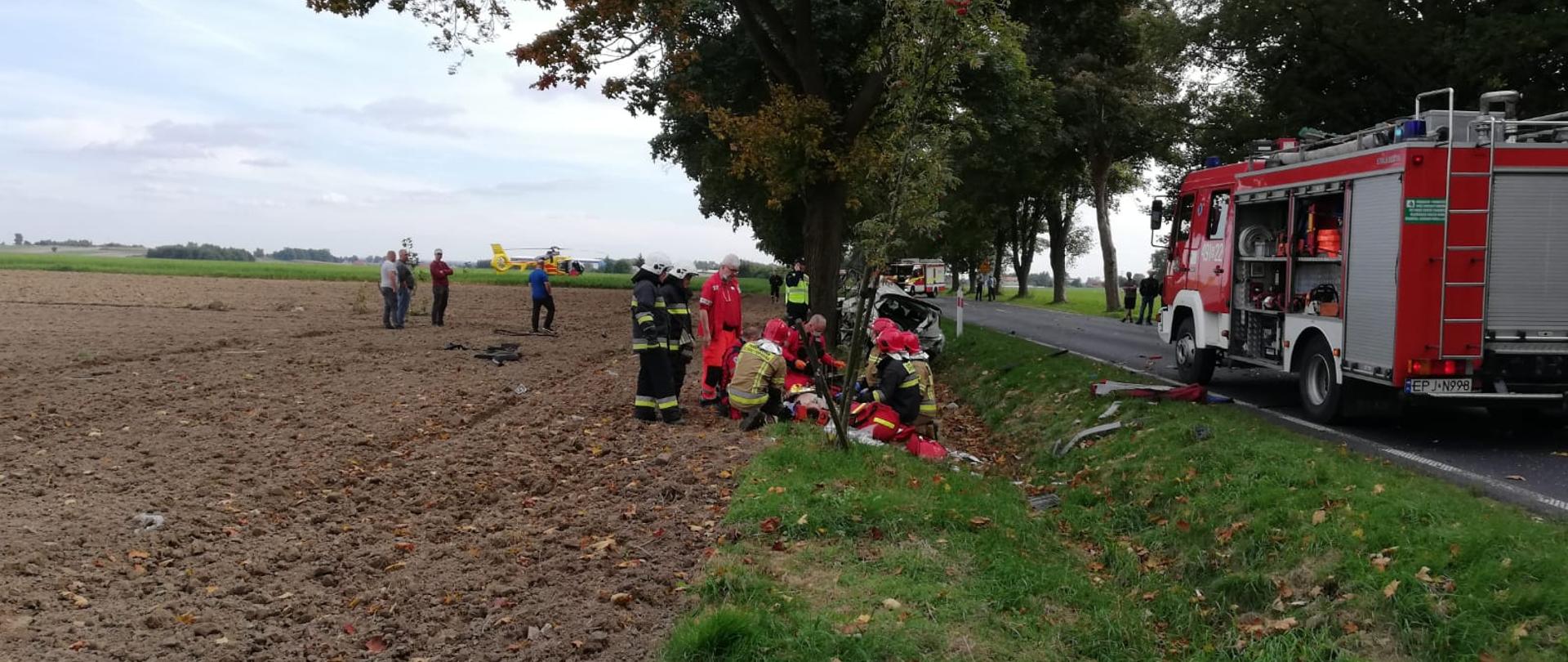 Strażacy i ratownicy udzielają pomocy poszkodowanemu w wypadku drogowym
