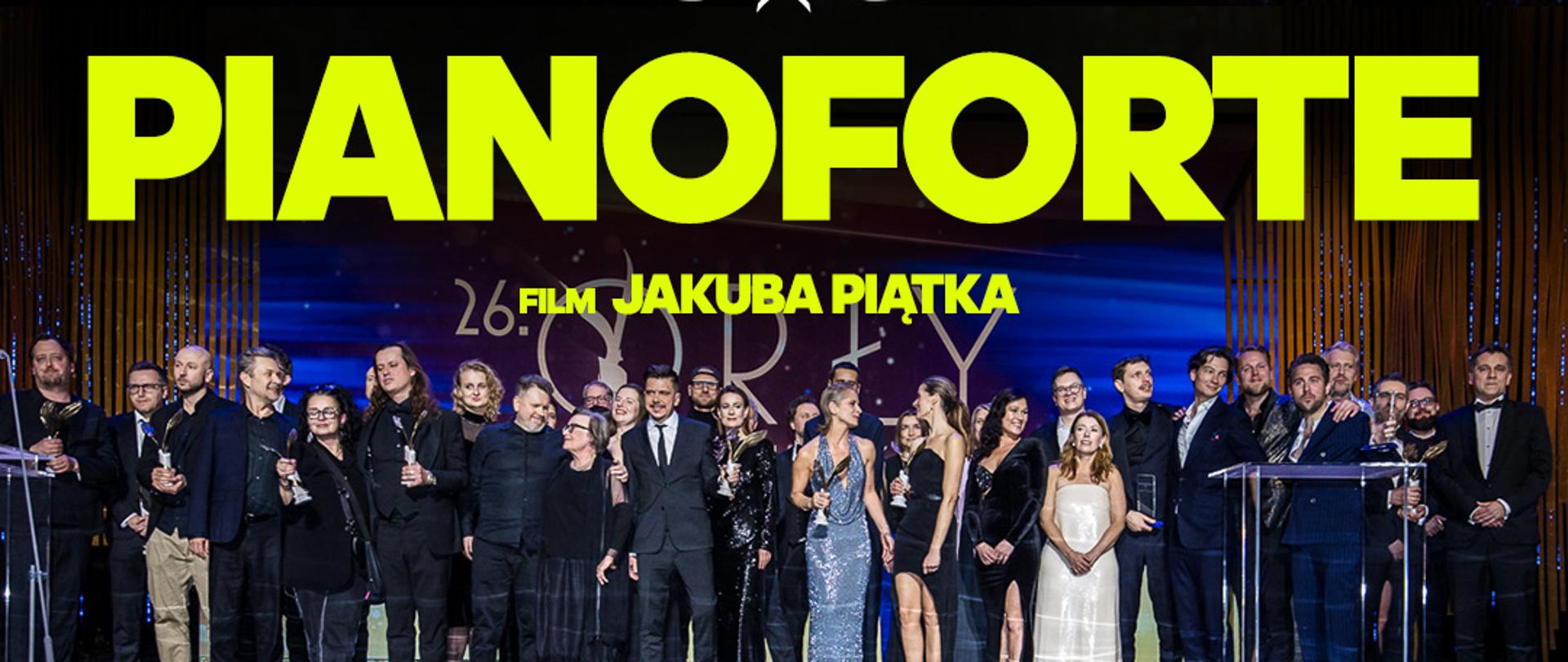 Wykonawcy filmu na scenie stoją w kilku rzędach. Powyżej nich Duży napis PIANOFORTE film Jakuba Piątka