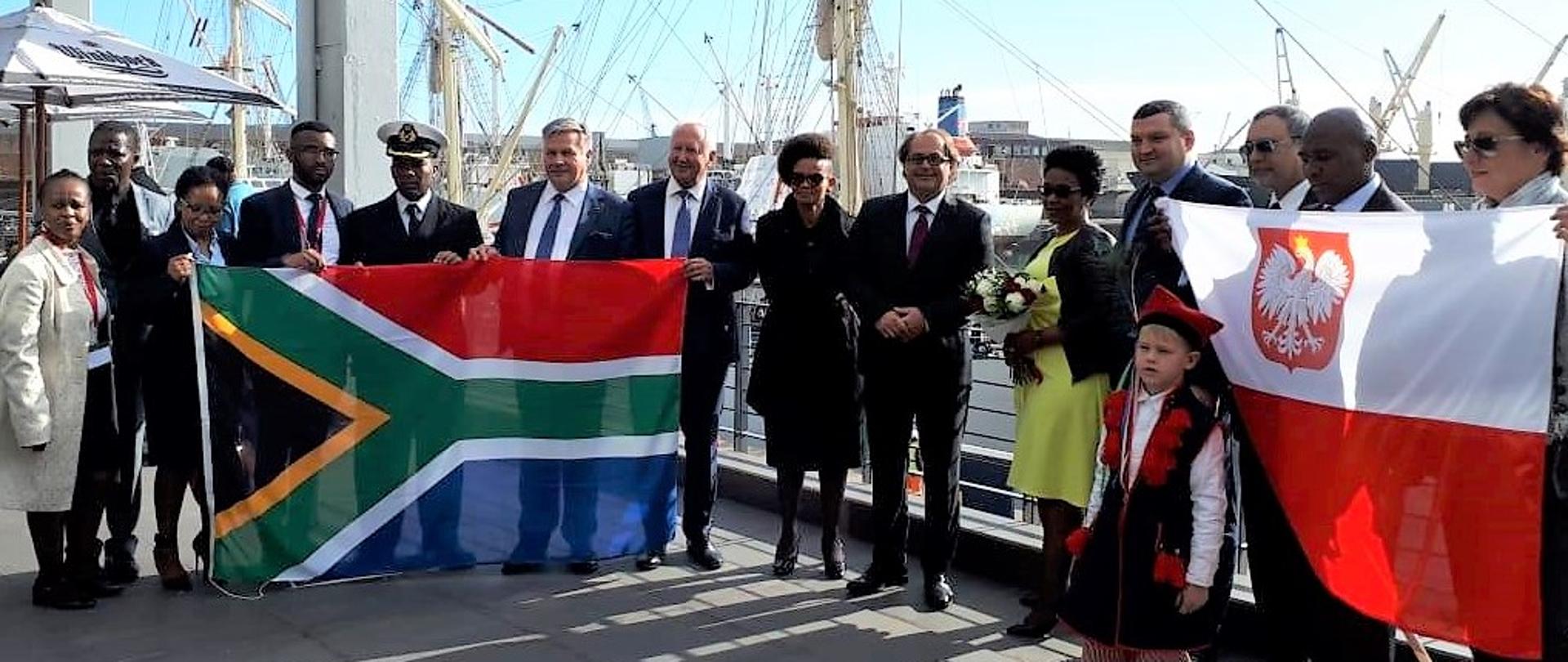 Minister Marek Gróbarczyk wraz z przedstawicielami oficjeli polskich oraz Rep. Południowej Afryki pozują do zdjęcia na statku Daru Młodzieży z flagami obu państw