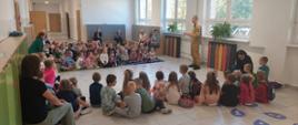 Zdjęcie przedstawia dzieci siedzące na ziemi oraz opiekunów siedzących na ławce, którzy słuchają strażaka.