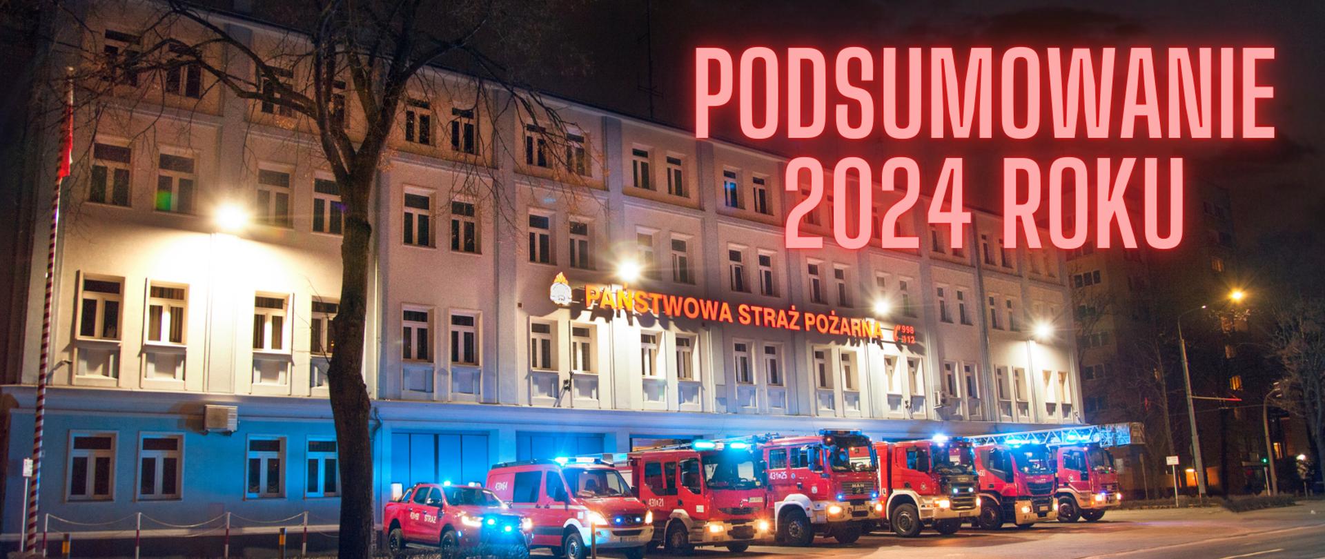 Budynek KM PSP w Gdyni. Przed nim wystawiono 7 wozów strażackich. Samochody mają włączone niebieskie światła alarmowe. Na budynku widnieje duży podświetlony napis Państwowa Straż Pożarna.