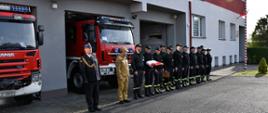Na zdjęciu widzimy komendanta oraz strażaków stojących w szeregu, jeden z nich trzyma złożoną flagę państwową.