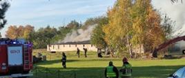 Na zdjęciu strażacy i policjant na tle palącej się hali