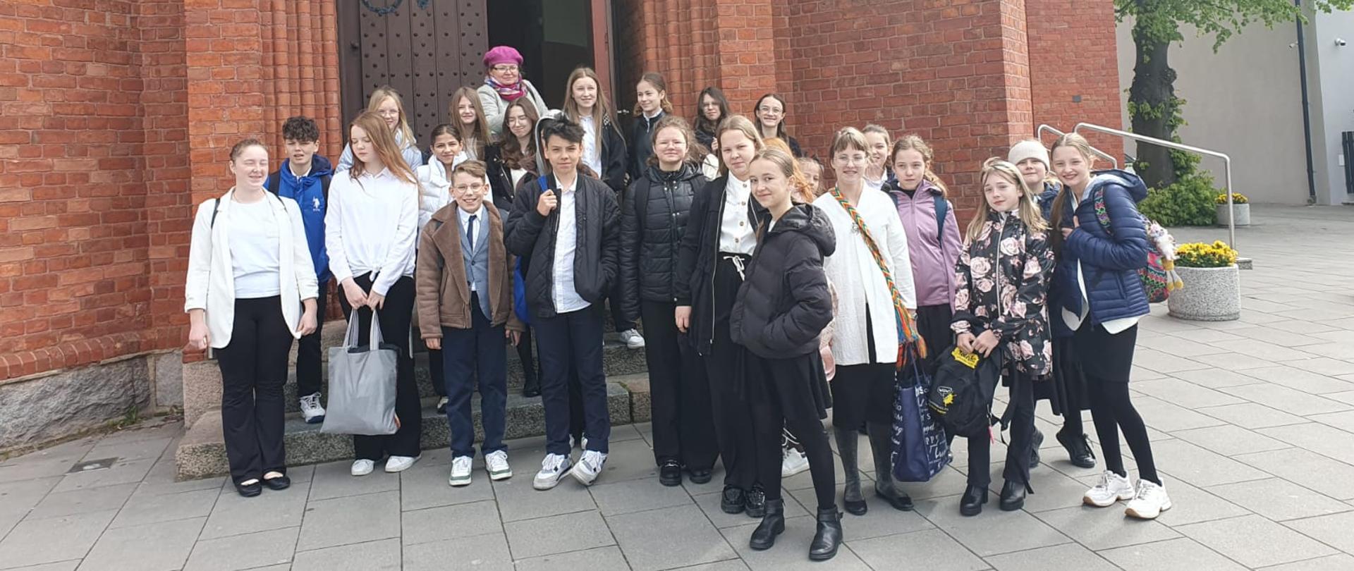 Na zdjęciu grupa uczniów. Wszyscy stoją na chodniku przed kościołem. 