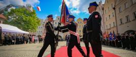 Na zdjęciu widać strażaków przekazujących sobie sztandar. Zdjęcie wykonane w dzień podczas Wojewódzkich Obchodów Dnia Strażaka. Strażacy w umundurowaniu galowym. 