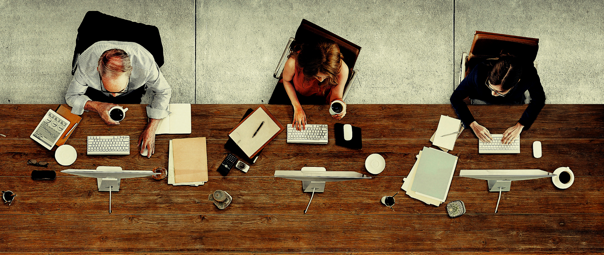 Trzy osoby siedzące przy biurkach i pracujące na komputerach.