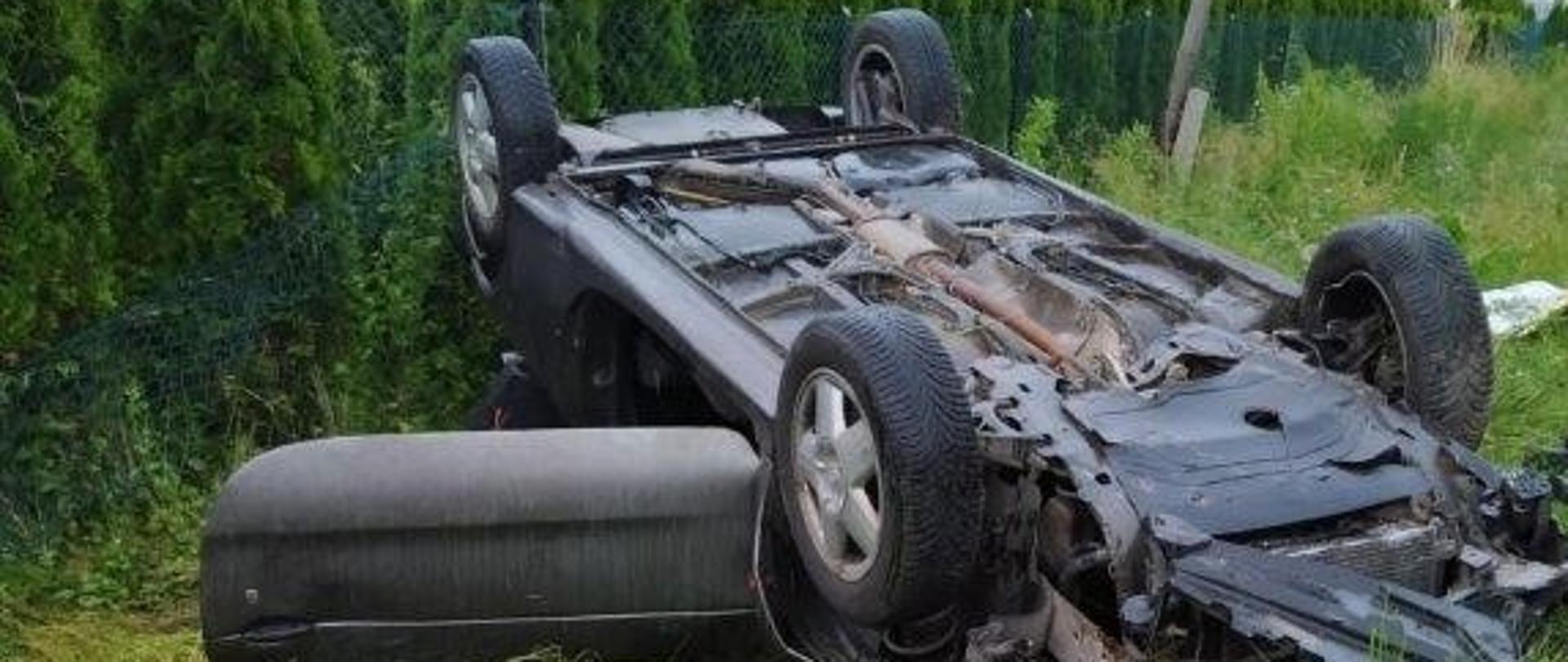 Zdjęcie przedstawia samochód osobowy leżący na dachu poza drogą