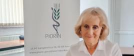 Kobieta siedzi przed laptopem. Ma na sobie białą koszulę z napisem „PIORiN”, w tle za nią stoi biało granatowy baner z logo instytucji.