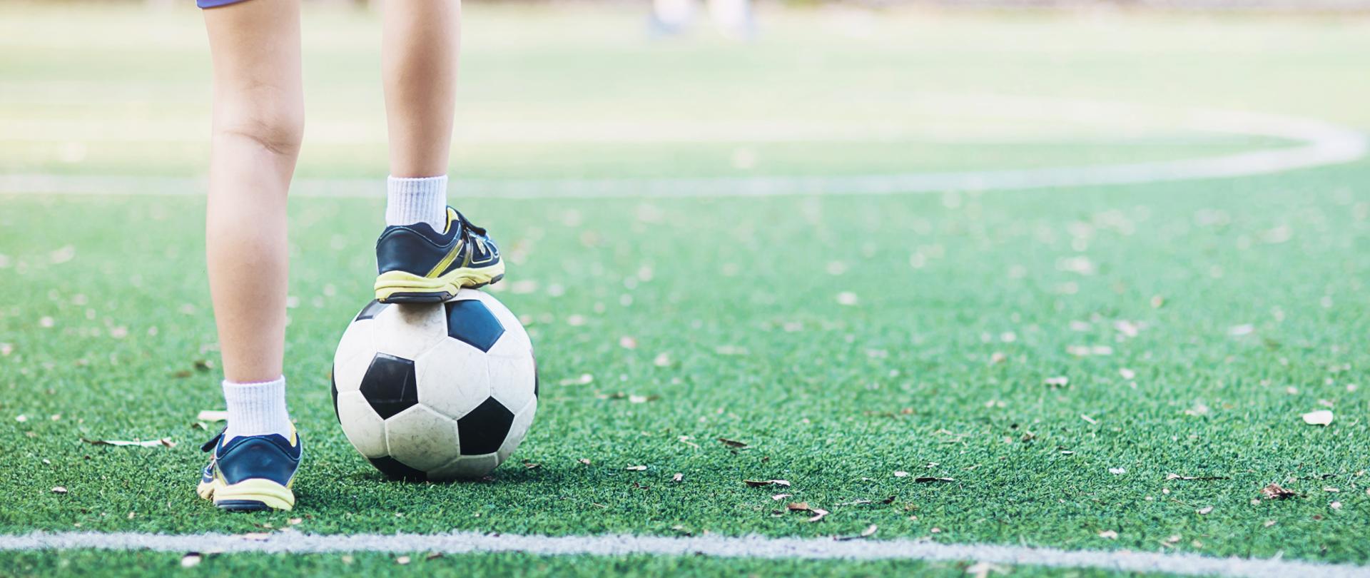 Chłopiec stojący na piłce, na boisku piłkarskim.