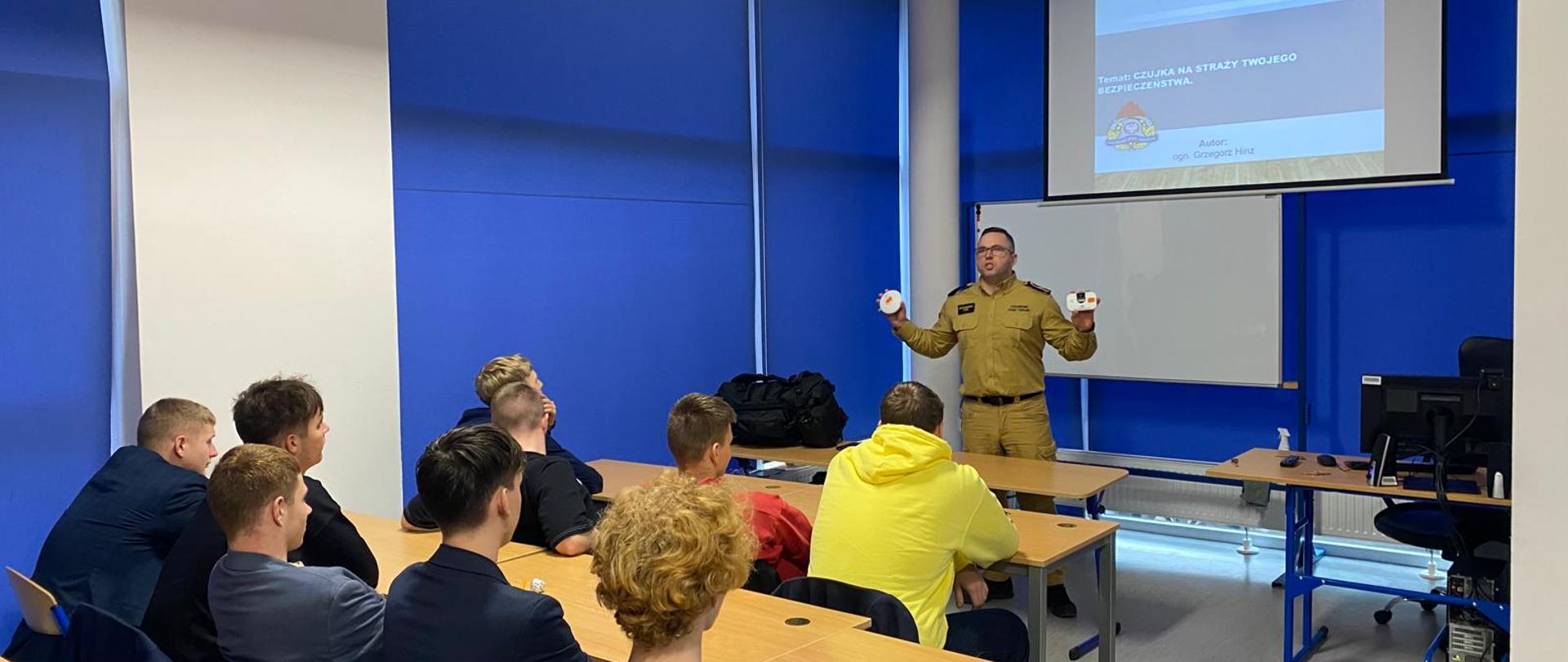 Funkcjonariusz pokazuje czujkę tlenku węgla i czujkę dymu