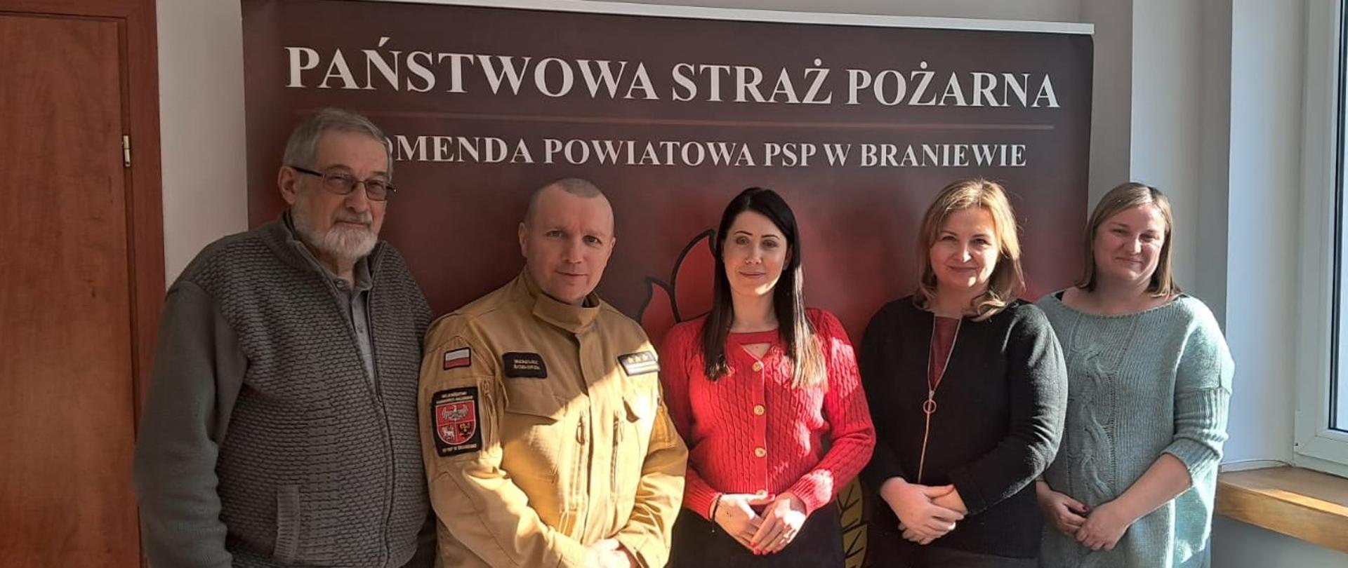 Rozmawiano o modernizacji strażnicy OSP Braniewo. W tle ścianka z napisem państwowa straż pożarna. Na zdjęciu pięć osób, prawej trzy kobiety.