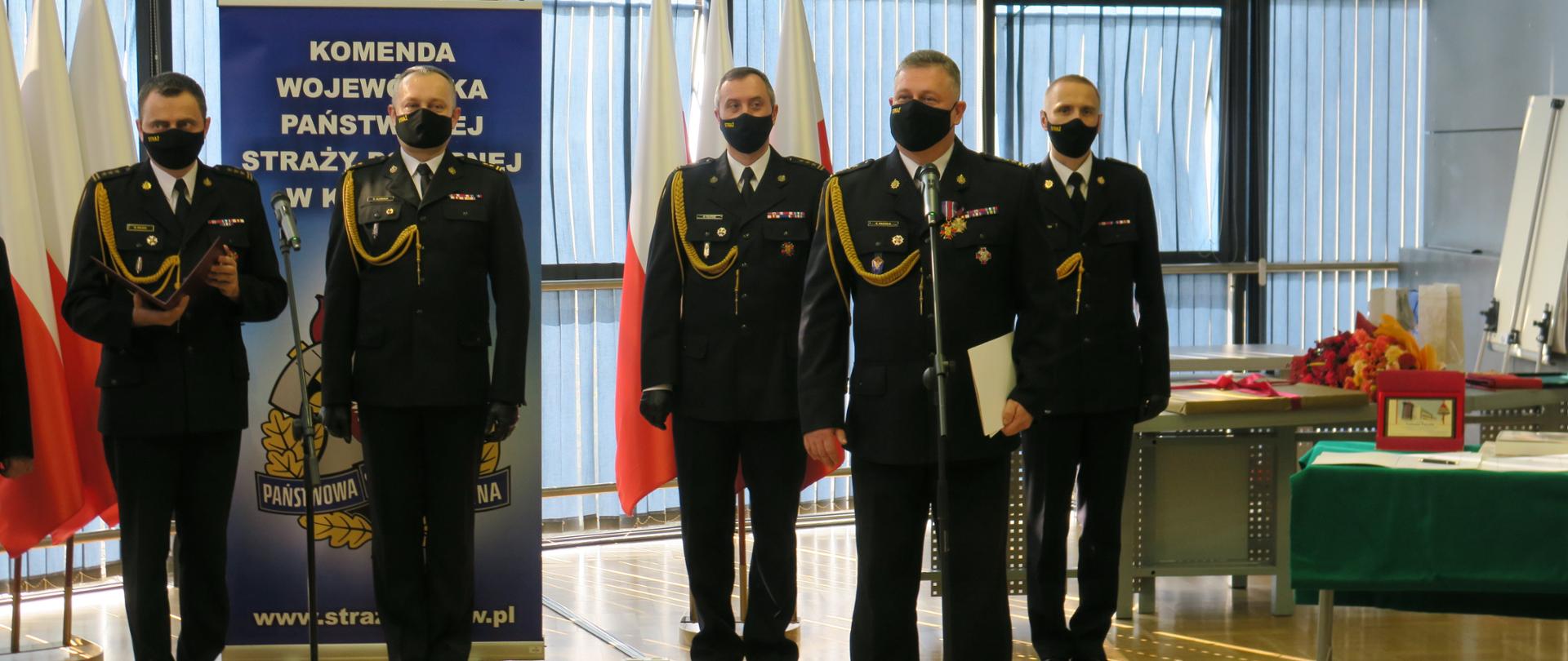 Strażak odchodzący na emeryturę przemawia przy mikrofonie. Za nim stoją komendanci.