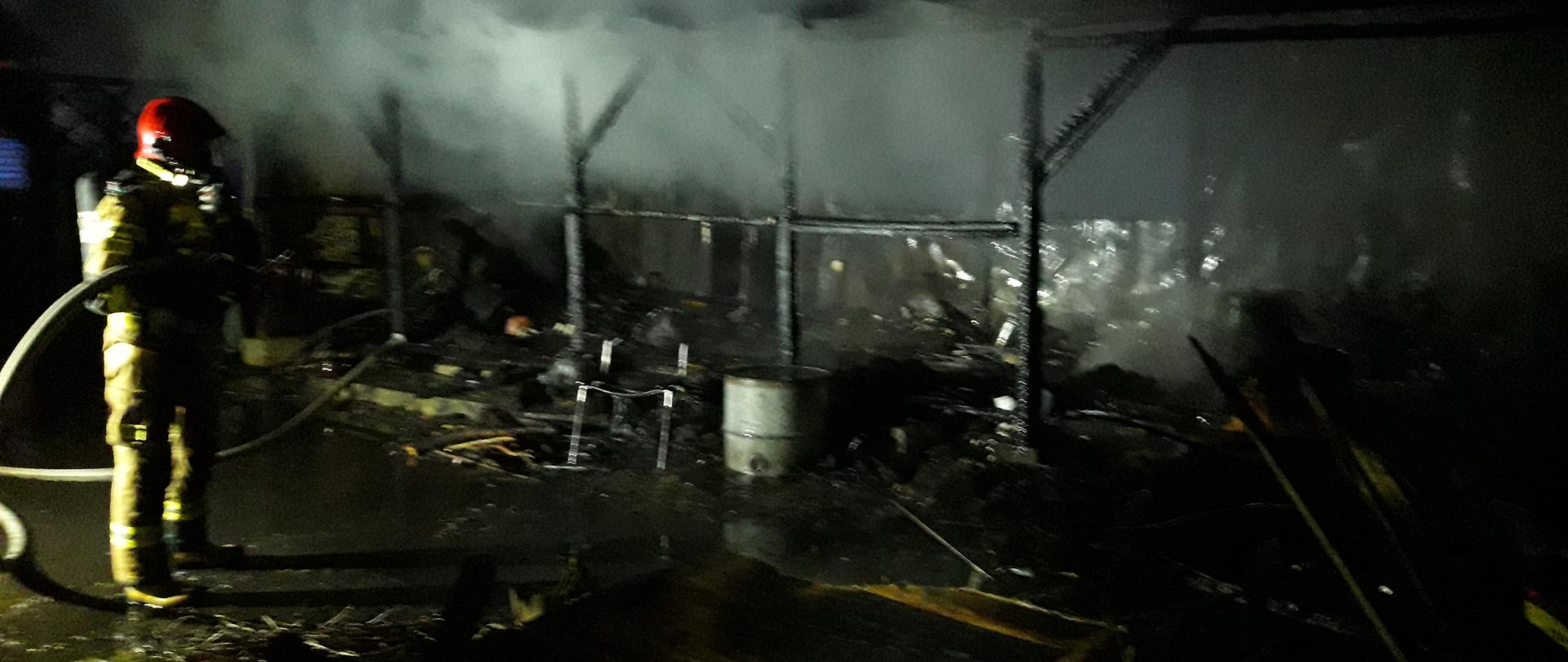 Noc, spalony wagon, po lewej stronie strażak.