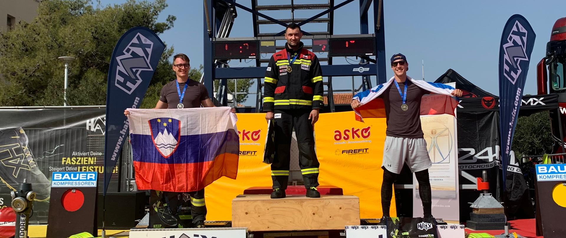 Trzech funkcjonariuszy stojących na podium z medalami. W tle wieża zawodów.