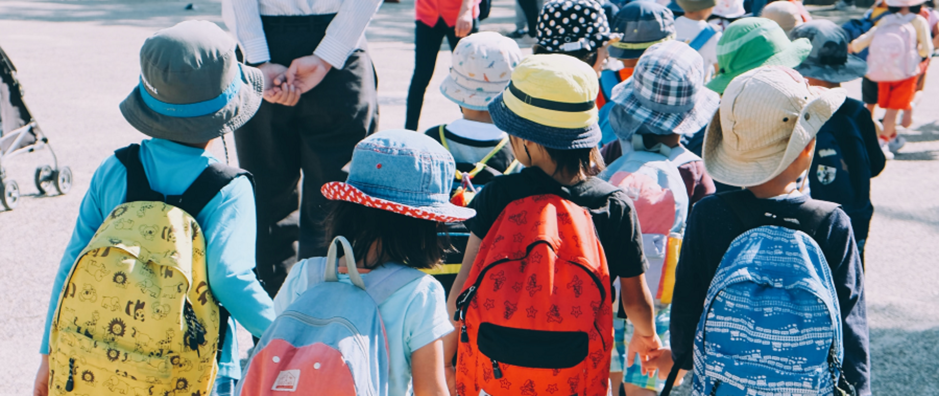 Zdjęcie przedstawiające dziewczynkę w wieku szkolnym - zdjęcie ukazujące grupkę uczniów z plecakami idących z nauczycielem