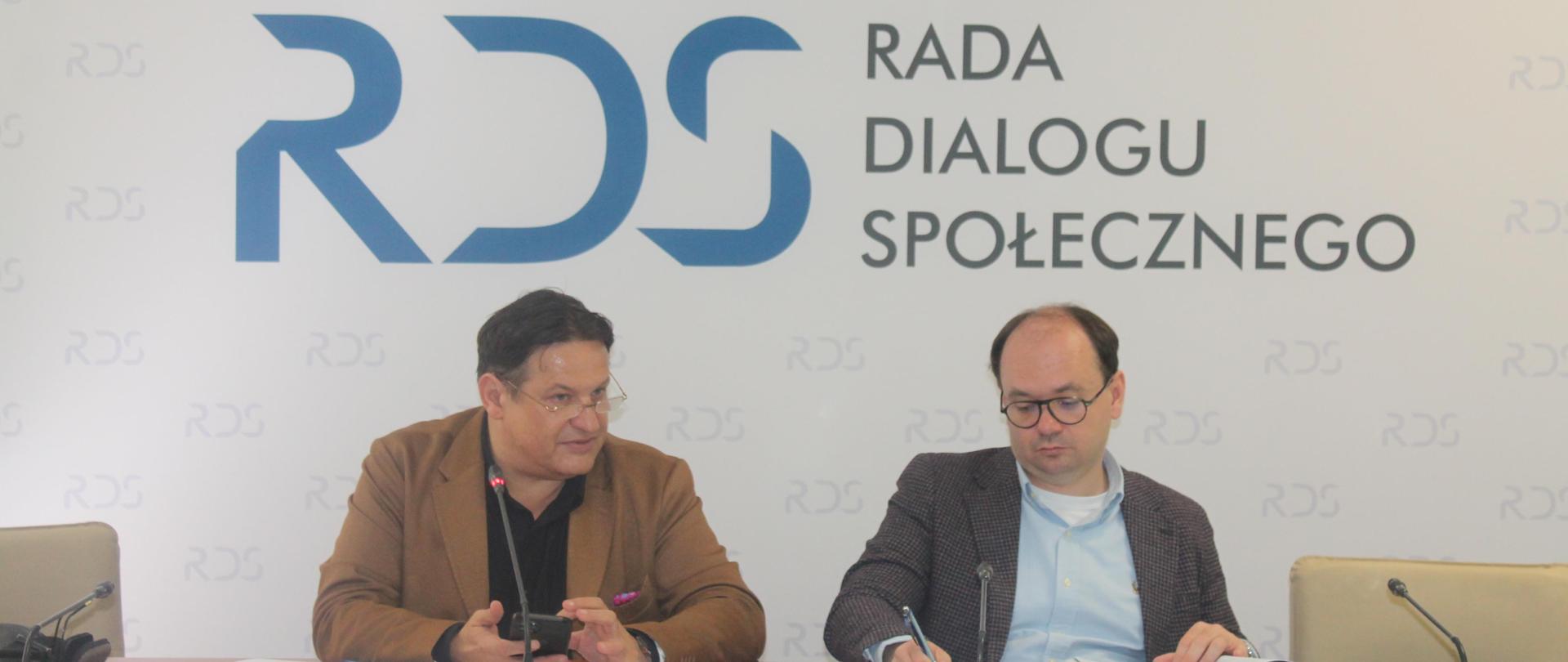 Na zdjęciu widnieje stół prezydialny za którym siedzą: Pan Sebastian Gajewski, Podsekretarz Stanu w Ministerstwie Rodziny, Pracy i Polityki Społecznej oraz Pan Jacek Męcina, Przewodniczący Zespołu. W tle widnieje baner z napisem Rada Dialogu Społecznego