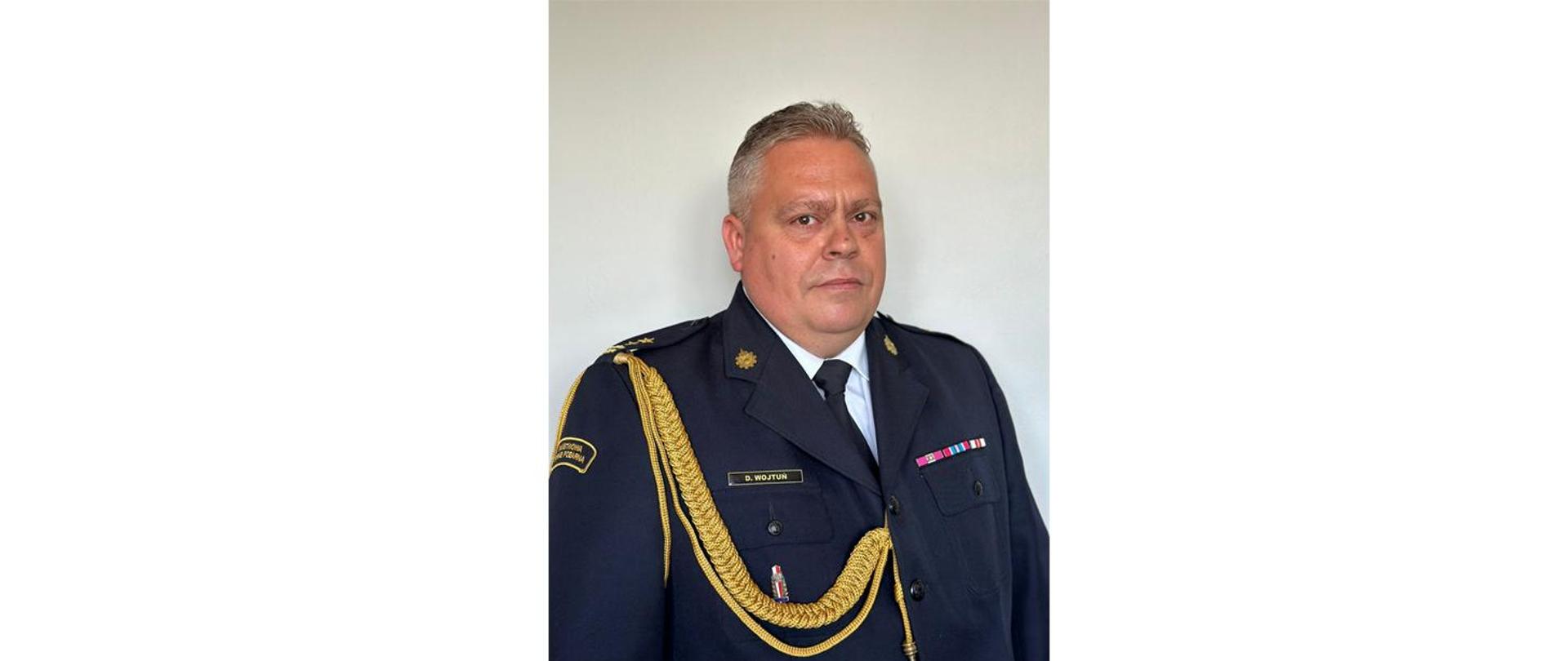 Zdjęcie portretowe Komendanta Powiatowego Państwowej Straży Pożarnej w Krośnie Odrzańskim (bryg. Dariusz Wojtuń) na jasnym tle w mundurze galowym.