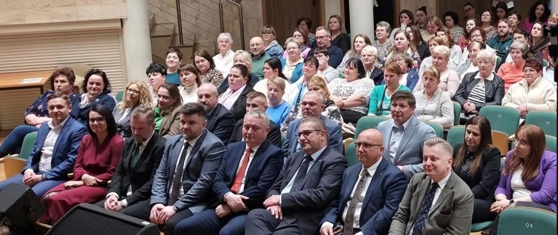 Na auli znajduje się kilkadziesiąt osób, które siedząc na krzesłach z uwagą słuchają wygłaszanych prelekcji.
