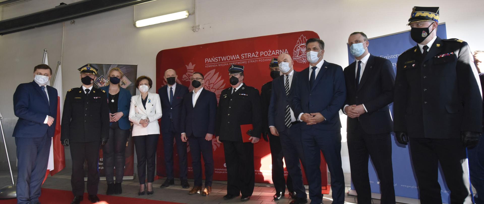 grupa ludzi stoi w szeregu, w tle czerwony baner, przed nimi czerwony dywan