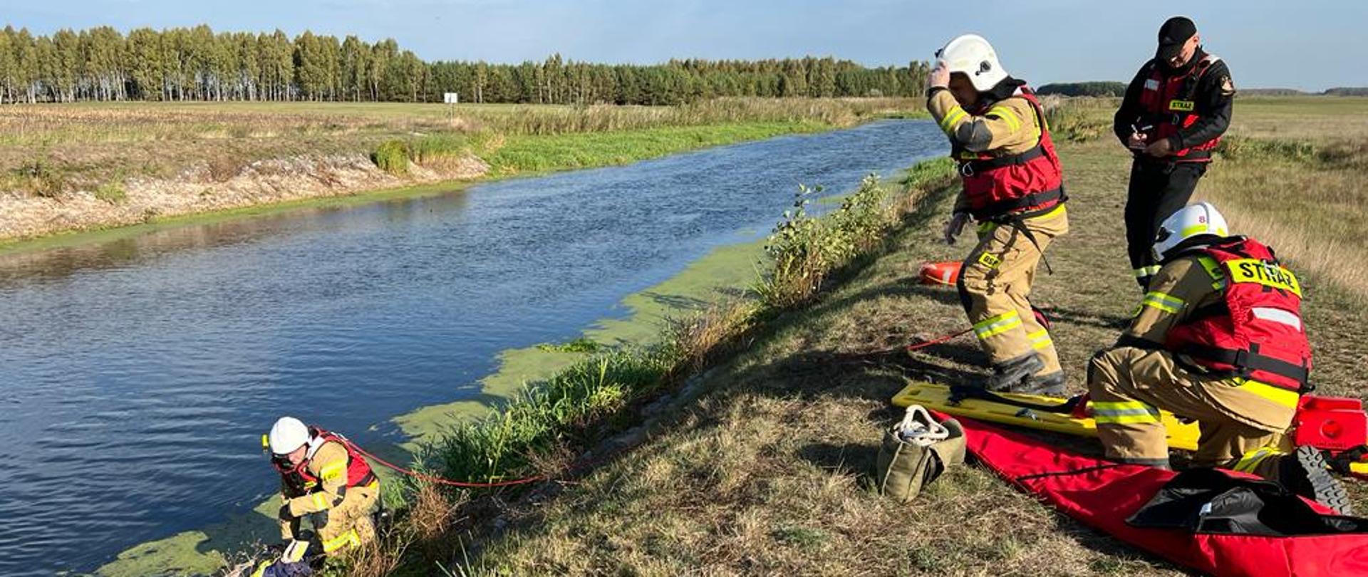 Druhowie OSP nad brzegiem rzeki w trakcie ćwiczeń