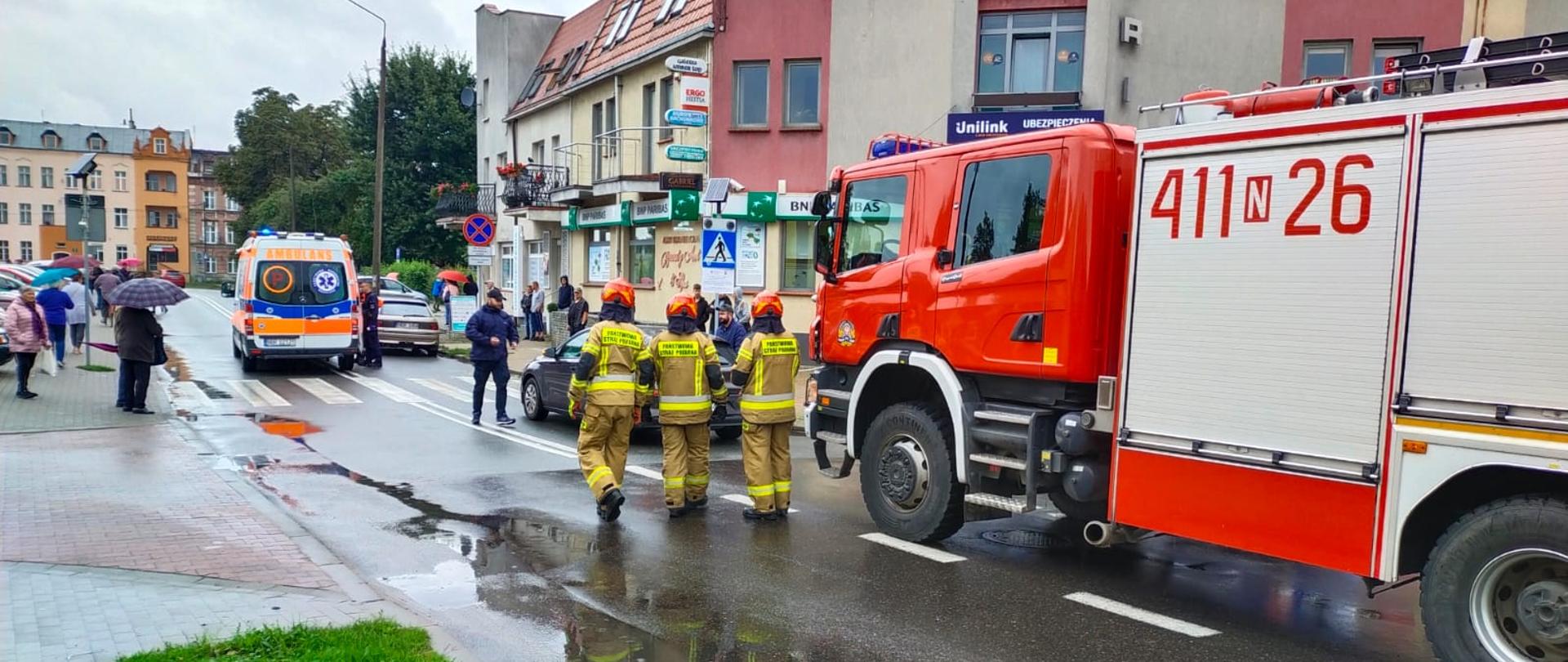 Na drodze stoją strażacy i samochody służb ratowniczych.