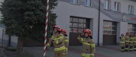 Zdjęcie przedstawia strażaków w ubraniu specjalnym, którzy wciągają flagę na maszt.