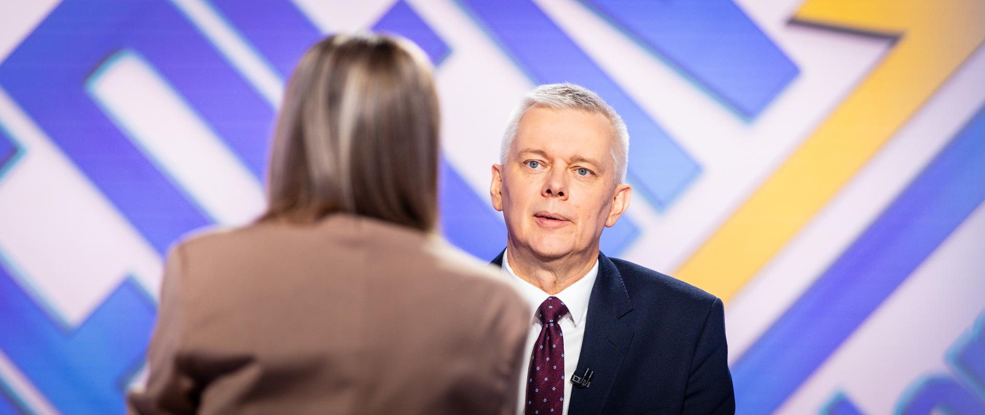 Na zdjęciu widać wnętrze studia TVN24. Przy stole siedzą dwie osoby: minister Tomasz Siemoniak (po prawej) oraz redaktor Arleta Zalewska (po lewej, siedzi tyłem do obiektywu). W tle niebieski napis na białym tle - nazwa programu "Jeden na jeden" z żółtym podkreśleniem.