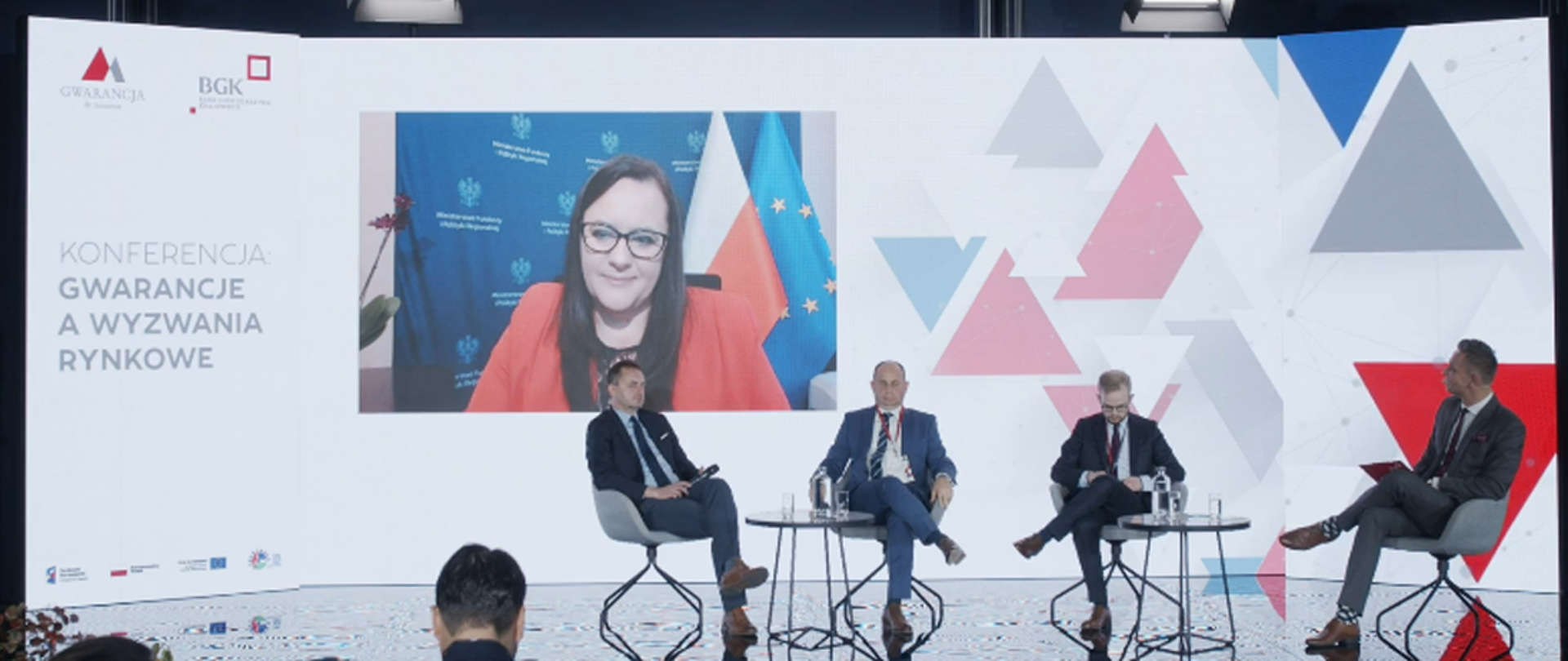 Na scenie siedzi czterech mężczyzn. Za nimi na ekranie wiceminister Małgorzata Jarosińska-Jedynak.