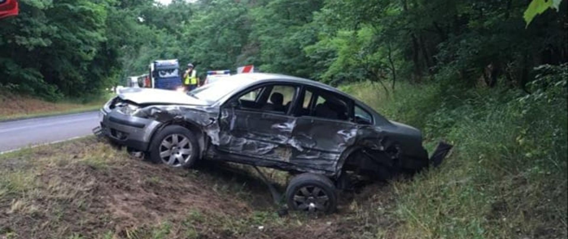 Zdjęcie przedstawia rozbity samochód osobowy marki VW Passat znajdujący się w przydrożnym rowie. 