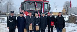 grupa osób stoi przed pojazdem pożarniczym który opleciony jest biało czerwoną wstęgą, zima