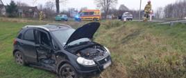 Po lewej na polu stoi czarny Fiat Sedici. W tle Fiat Seicento. Za nim Karetka pogotowia i radiowóz policyjny. 