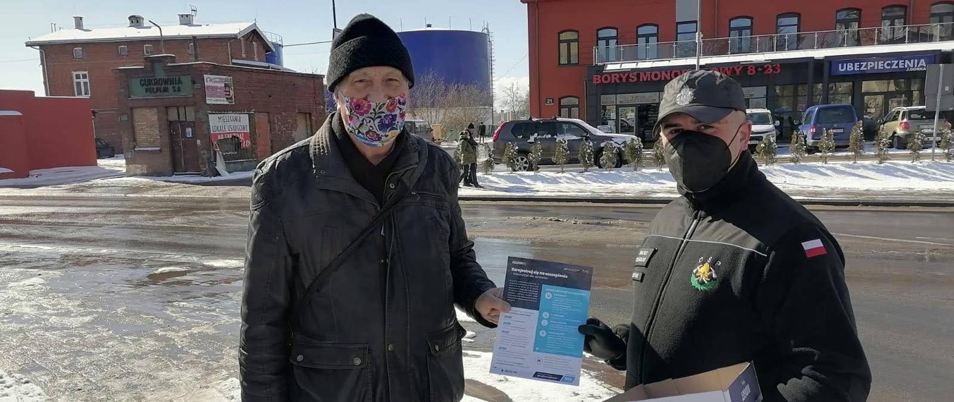 Strażak wręcza ulotkę informacyjną mężczyźnie.