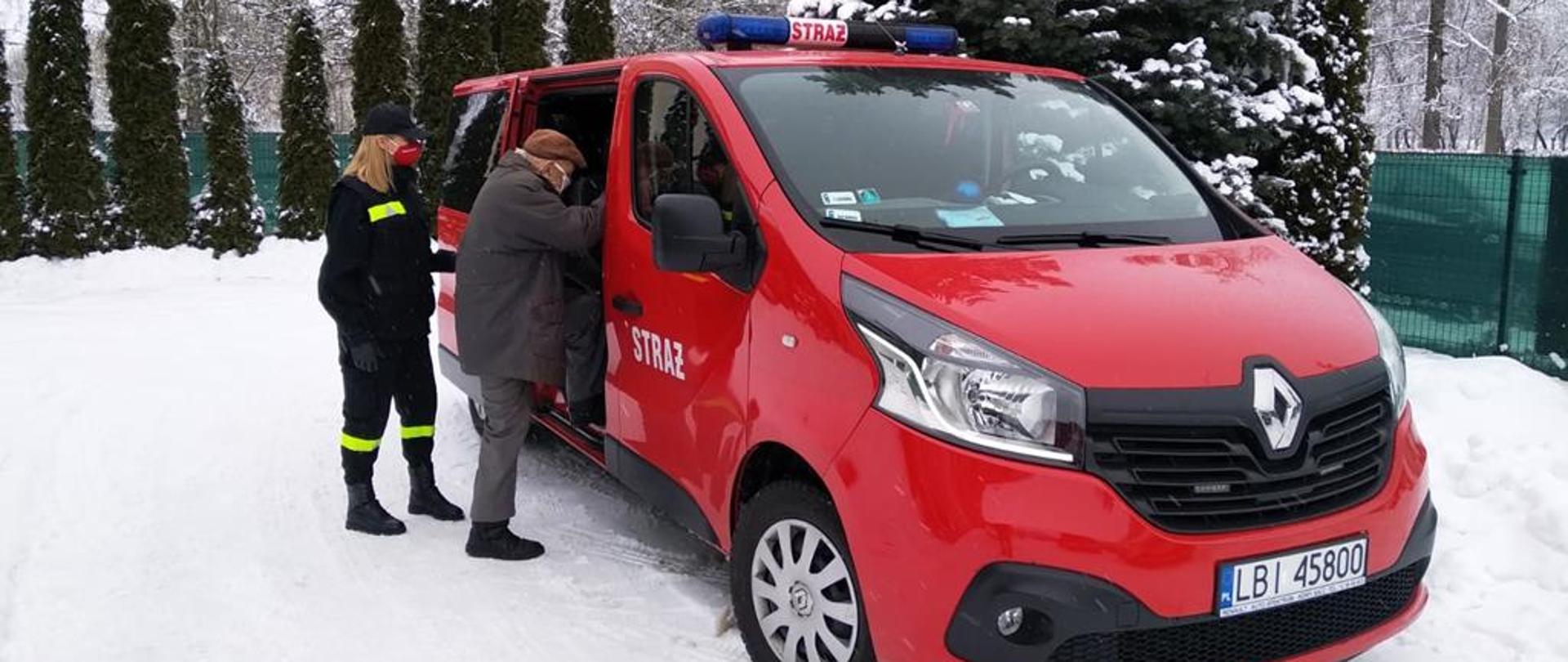 Kobieta strażak pomaga wejść starszemu panu do pojazdu OSP po zaszczepieniu. Straż pomaga w dowozie potrzebujących do punktów szczepień