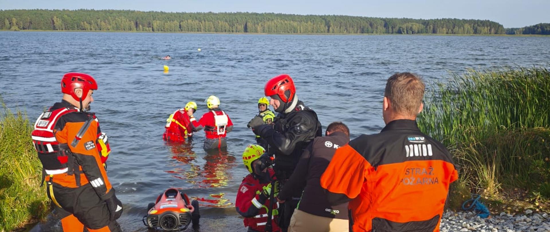 Strażacy podczas szkolenia praktycznego nad brzegiem Zalewu Koronowskiego. Uczestnicy ćwiczą wykorzystanie sprzętu ratowniczego oraz współpracę podczas działań na obszarach wodnych.