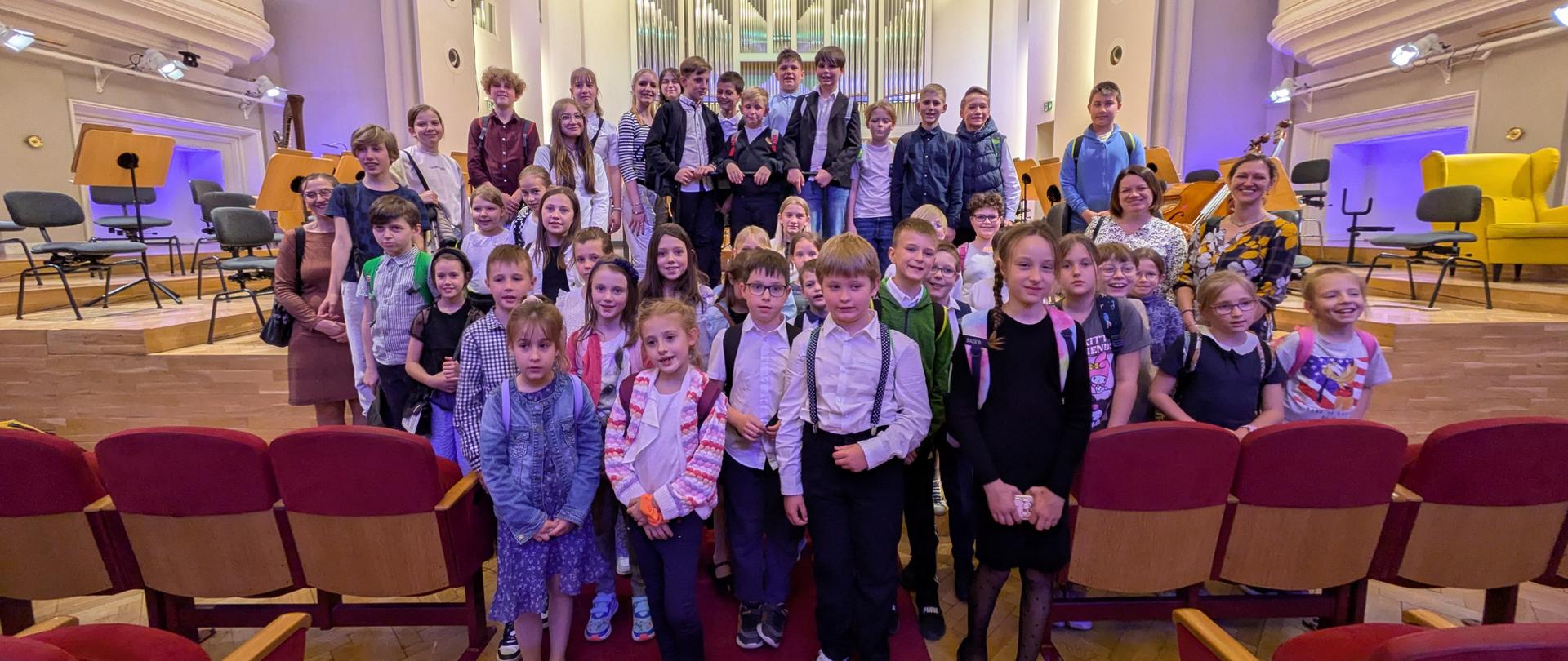 Uczniowie i opiekunowie stoją na scenie Filharmonii Śląskiej.