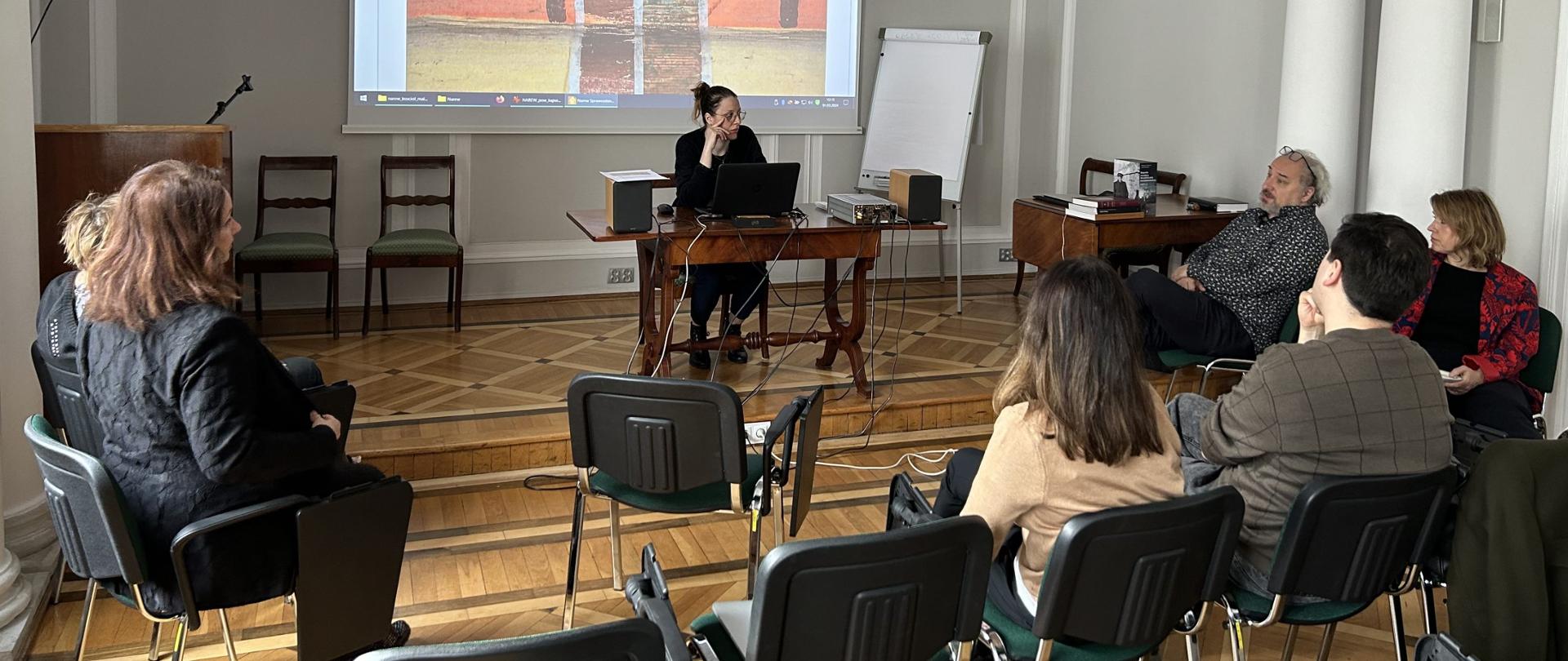 Spotkanie robocze redaktorów Katalogu Zabytków Sztuki w Polsce. Na zdjęciu 8 osób, 7 siedzących jako widownia, 1 prelegent.
