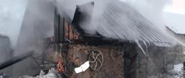 Zdjęcie przestawia wydobywanie się dymu z budynku murowanego krytego blachą na ścianie obiektu znajduje się koło stalowe