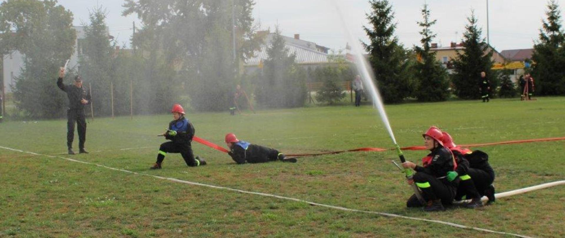 Dwie roty ratowniczo-gaśnicze podczas zawodów sportowo-pożarniczych. W tle widoczny strażak - sędzia zawodów
