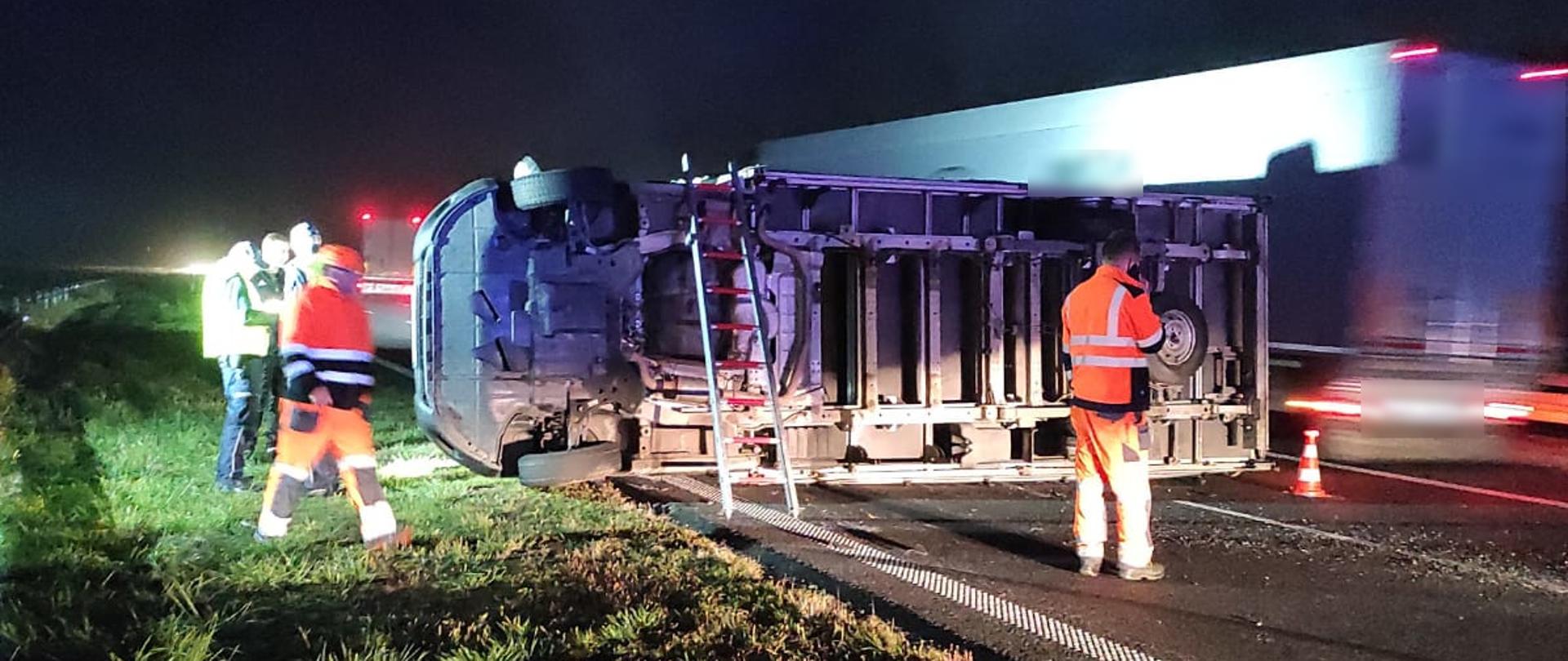 widoczne miejsce zdarzenia, uszkodzony pojazd leżący na boku, blokujący dwa pasy ruchu na trasie, oraz służby działające na miejscu