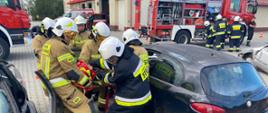 na zdjęciu strażacy w trakcie ćwiczenia egzaminacyjnego, w tle pojazdy i budynek strażnicy