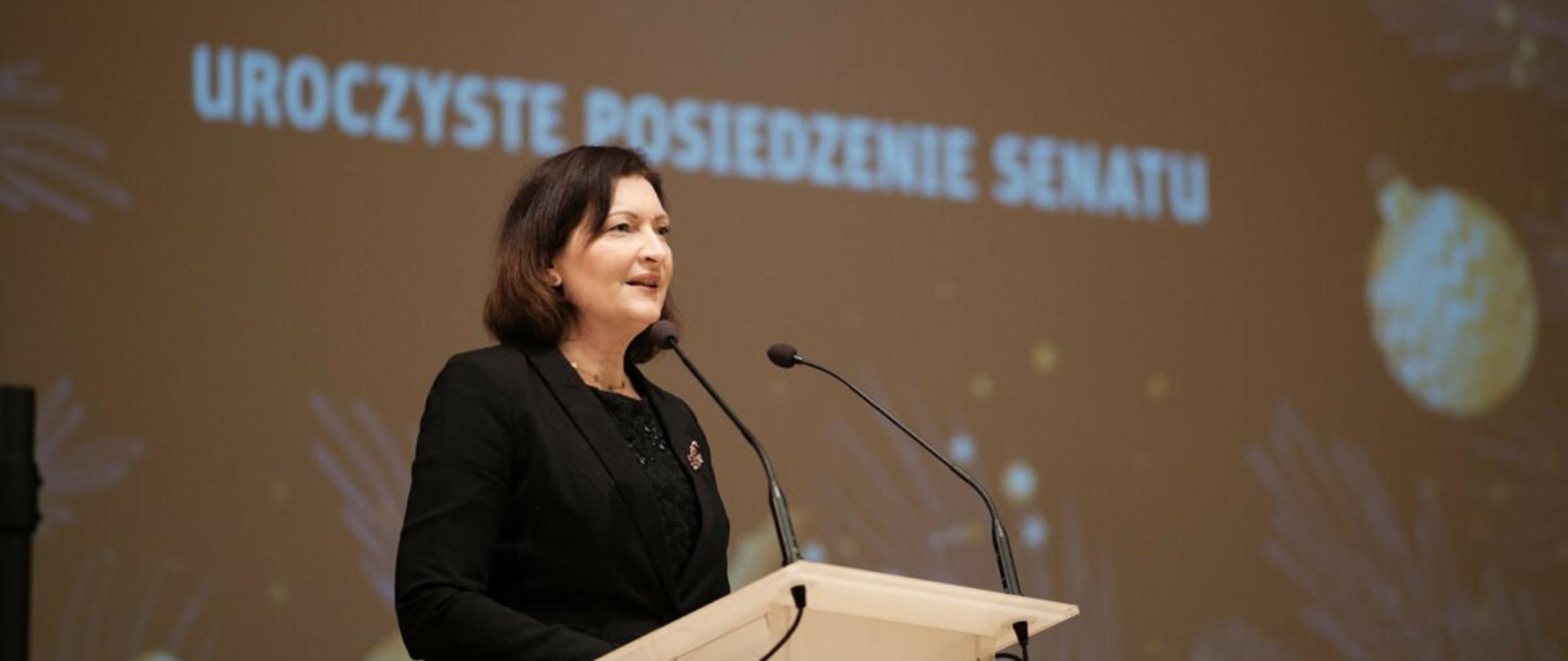 Wojewoda podkarpacki Ewa Leniart przemawia przy mównicy podczas posiedzenia Senatu Politechniki Rzeszowskiej. W tle napis uroczyste posiedzenie Senatu.