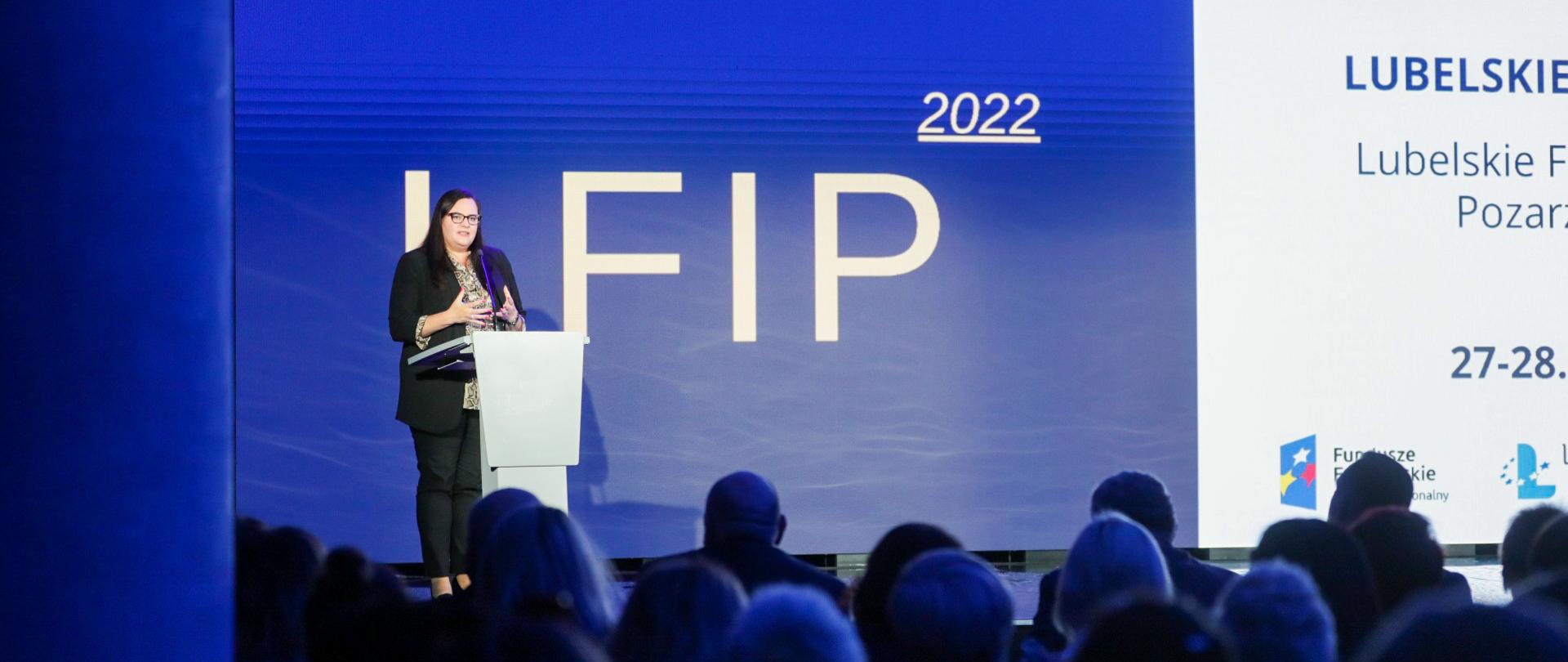 Na zdjęciu wiceminister Małgorzata Jarosińska-Jedynak stojąca na scenie przy mównicy. W tle ekran LED wyświetlający nazwę wydarzenia. U dołu widownia.