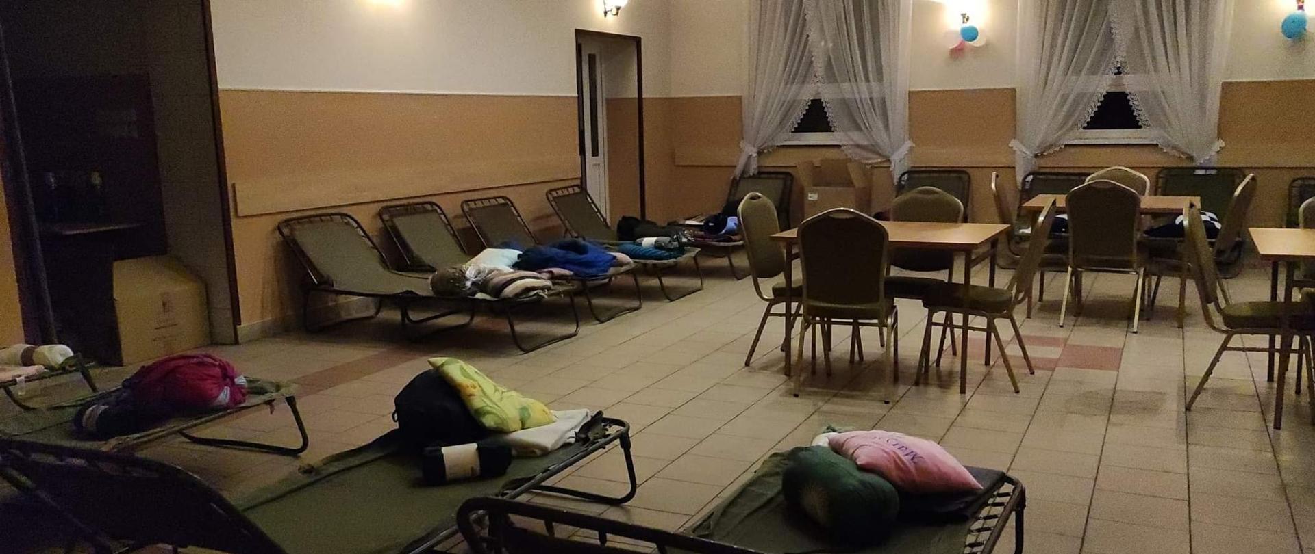 Zdjęcie przedstawia salę w remizie ze stołami i łózkami