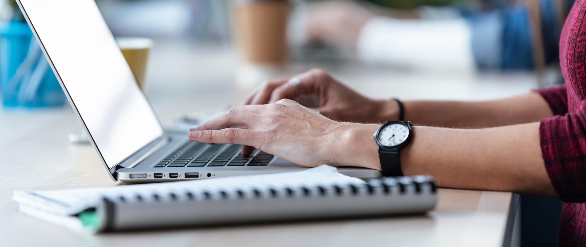 Ręce na klawiaturze laptopa. Widok z boku.